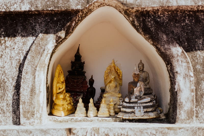 Little figurines of buddha sitting on the inside of a wall shrine. Learn how to make a shrine.
