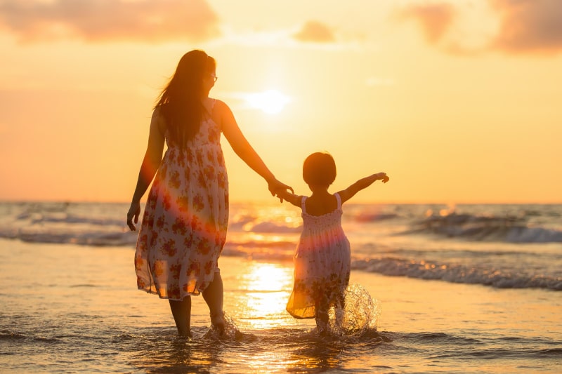 Mother and daughter holding hands at the beach during sunset. Grieving the loss of a mother