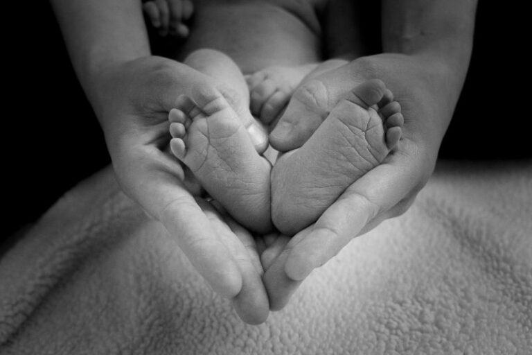 A picture of a mothers hands holding her babies feet in her hands in the form of a heart. Cope with the loss of a child